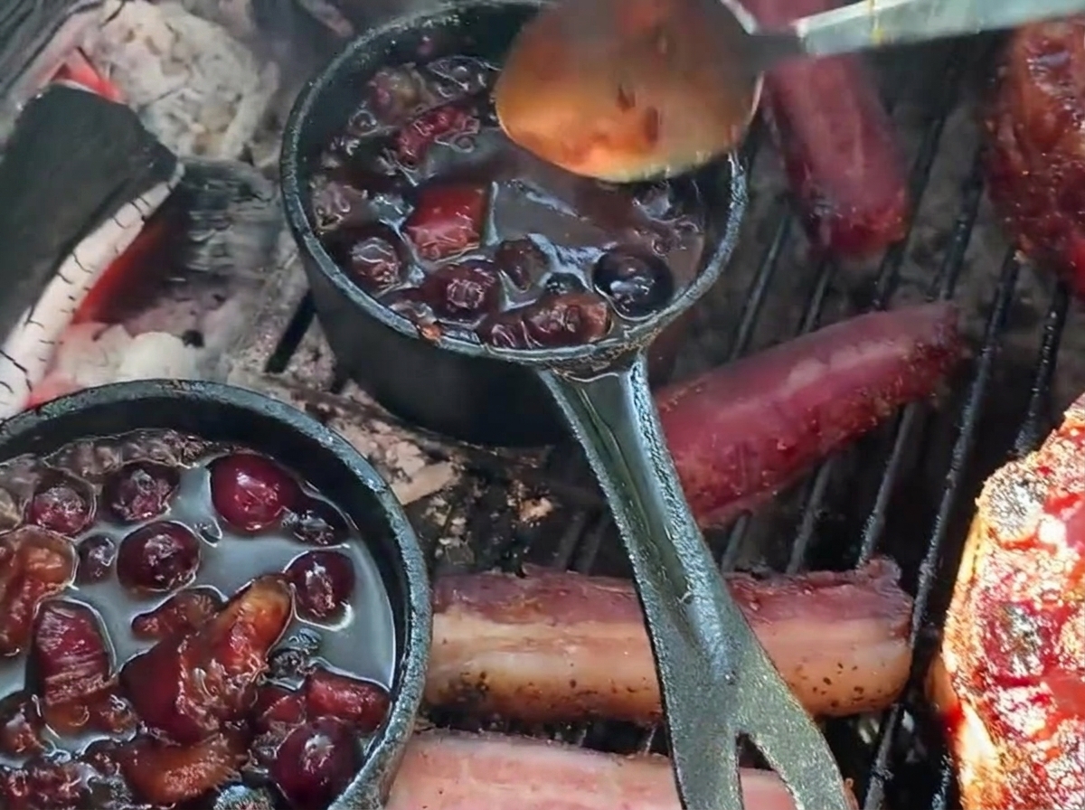 グリルの上のスタッフドリブカップに、小さな鋳鉄製の鍋から濃厚なブルーベリーBBQソースをスプーンでかけている様子。