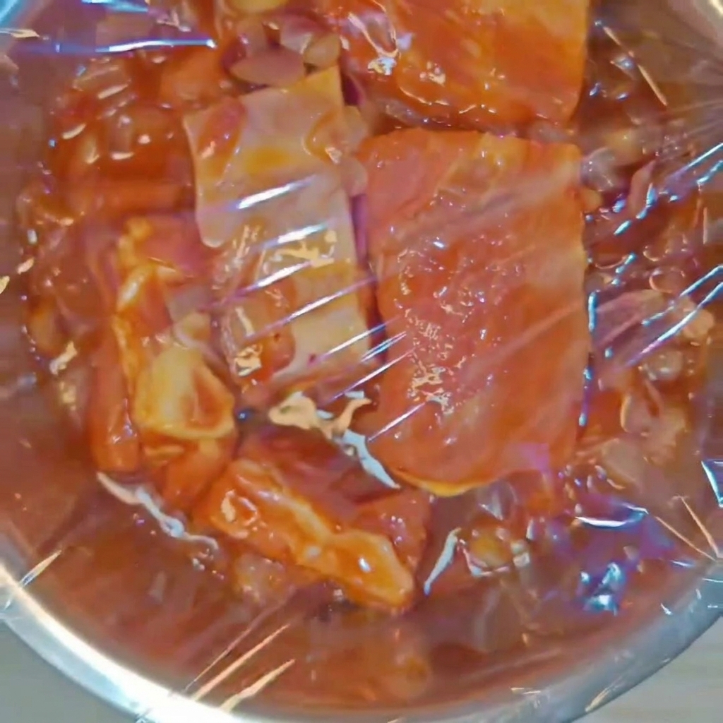 味付けしたポークリブが入ったステンレスボウルに、透明なラップをしっかりと密着させてかけている様子。