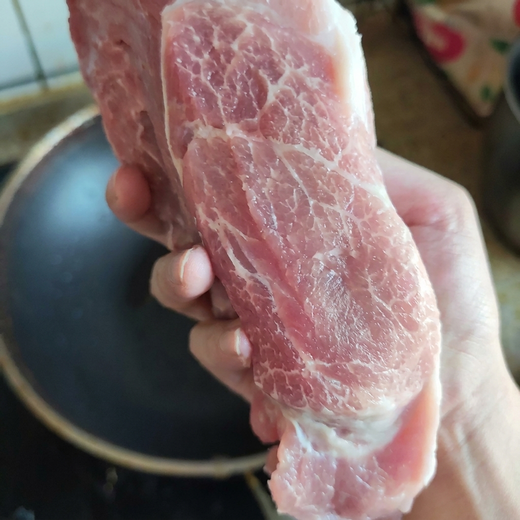 新鮮な質感と美しい脂身の入り具合がわかる、手で持ち上げられた生の豚肩ロースの塊肉。