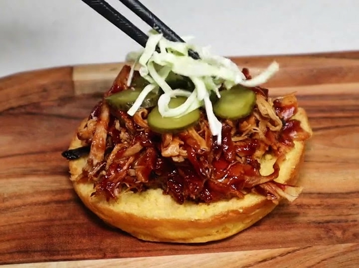 バーガーバンズの中のピクルスとプルドポークの上に、お箸で千切りキャベツのコールスローを乗せている様子。