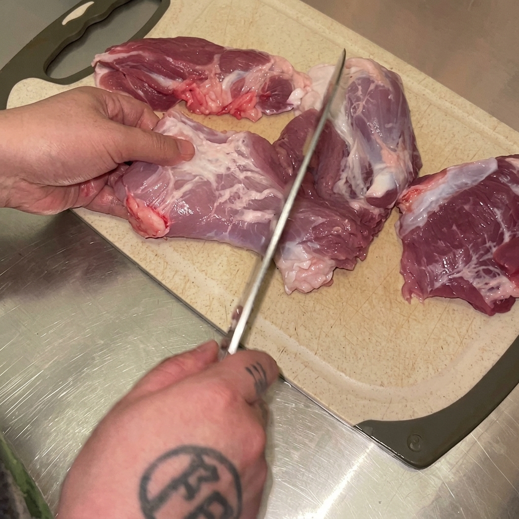 まな板の上で豚モモ肉を包丁で均等なサイズの塊に切り分けている様子。