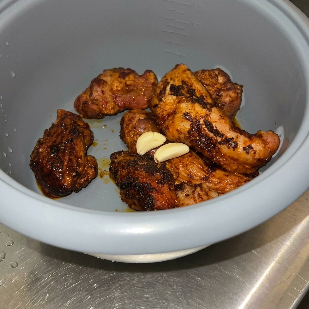 炊飯器の中の豚肉の上に、にんにく、ライム、ローリエ、シナモンを載せている様子。