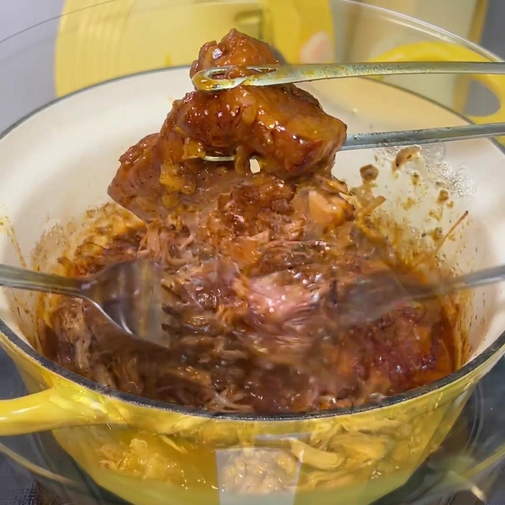 ボウルの中で、フォークを使って柔らかい豚肉を繊維状にほぐしている様子。