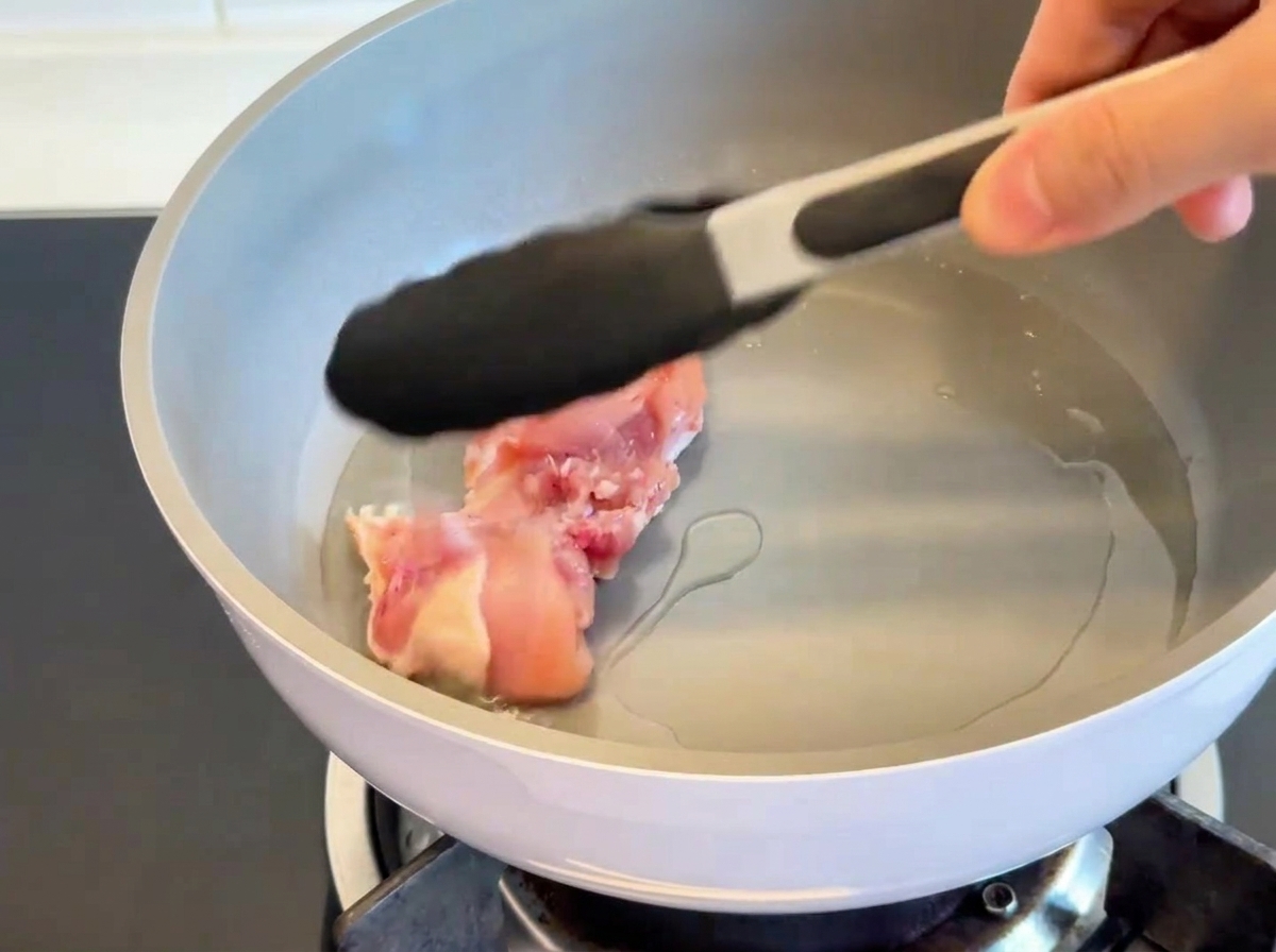 熱したフライパンで鶏もも肉を皮目から焼いている様子。皮がきつね色でパリッとしている。