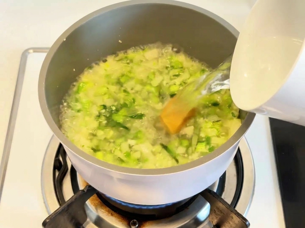 炒めた野菜とスープの素が入った鍋にお湯を注いでいる様子。