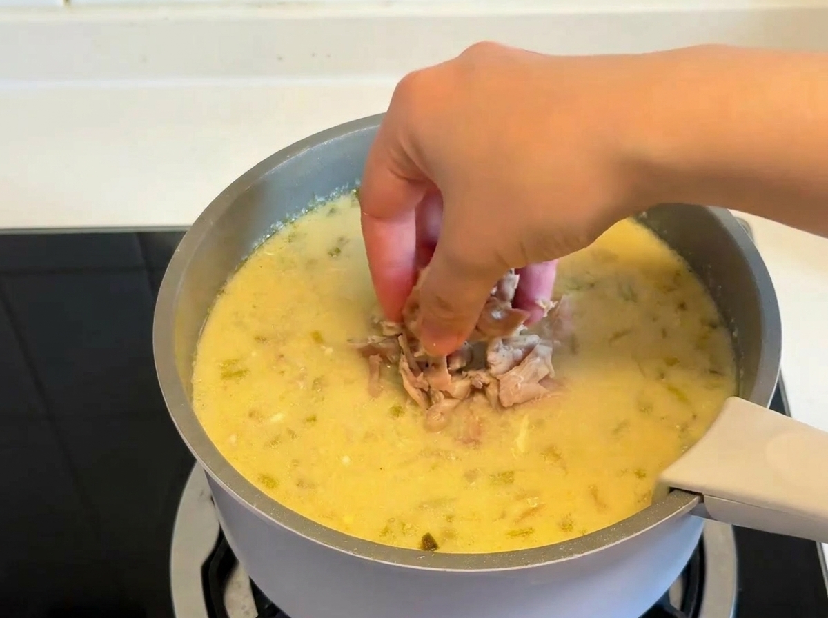 とろみのあるクリーミーなレモンスープの鍋に、ほぐした鶏肉を入れている様子。