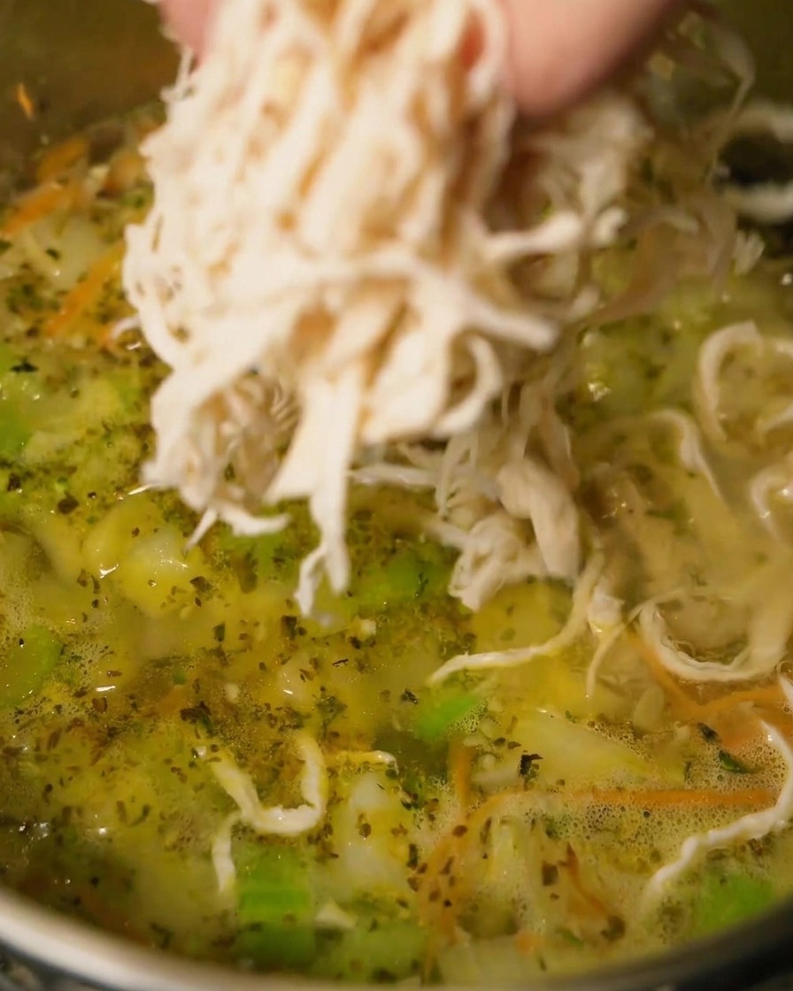軽く煮立ったスープに、ほぐした鶏肉を加えている様子。