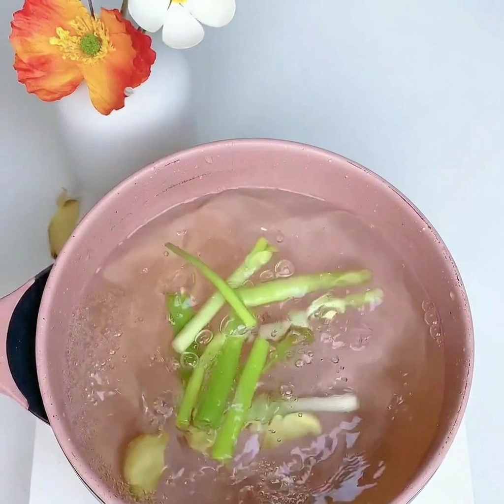 鍋でねぎ、生姜、八角と一緒に鶏もも肉を茹でている様子。