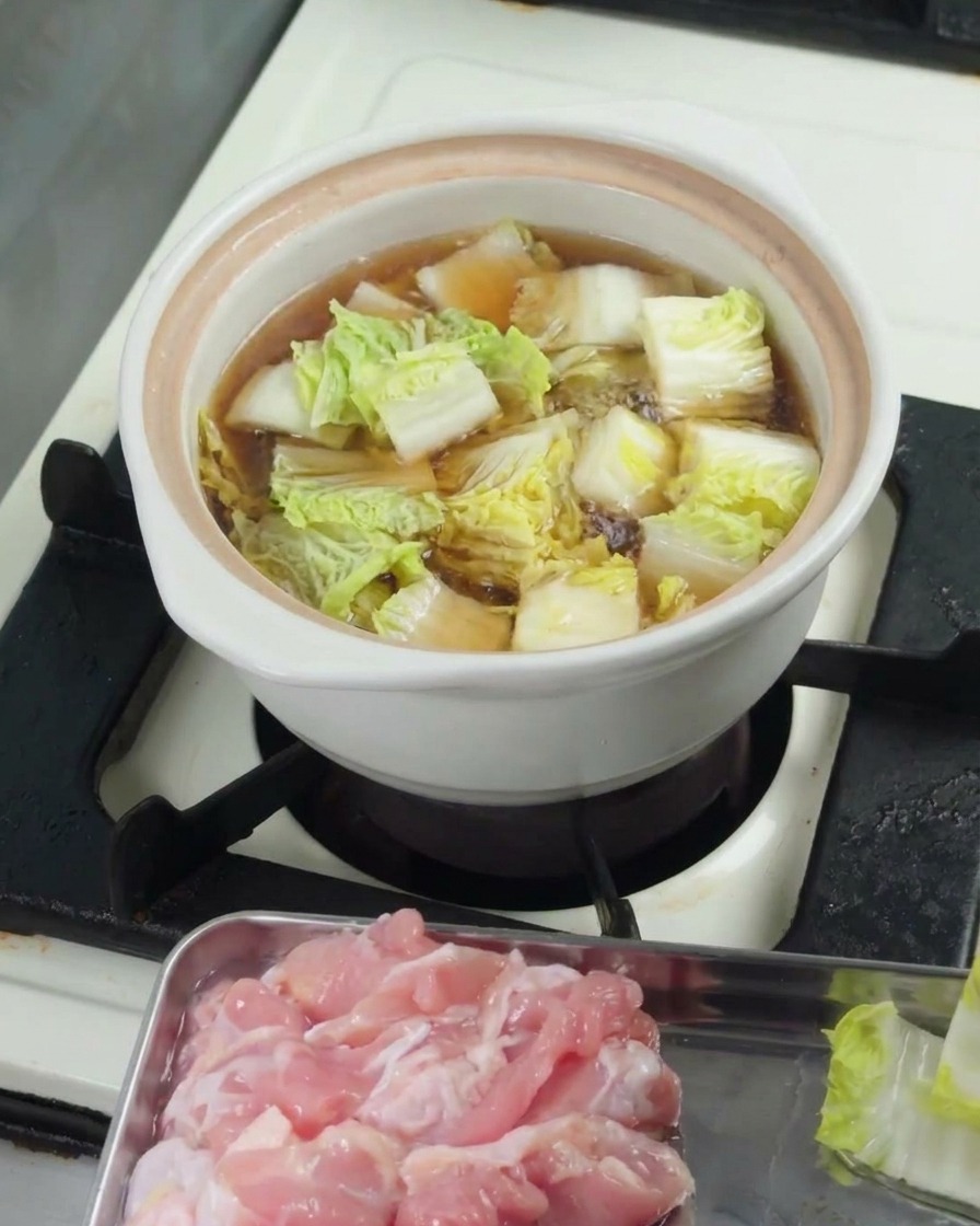 鍋の中のスープに刻んだチンゲン菜を入れ、蓋をして煮ている様子。