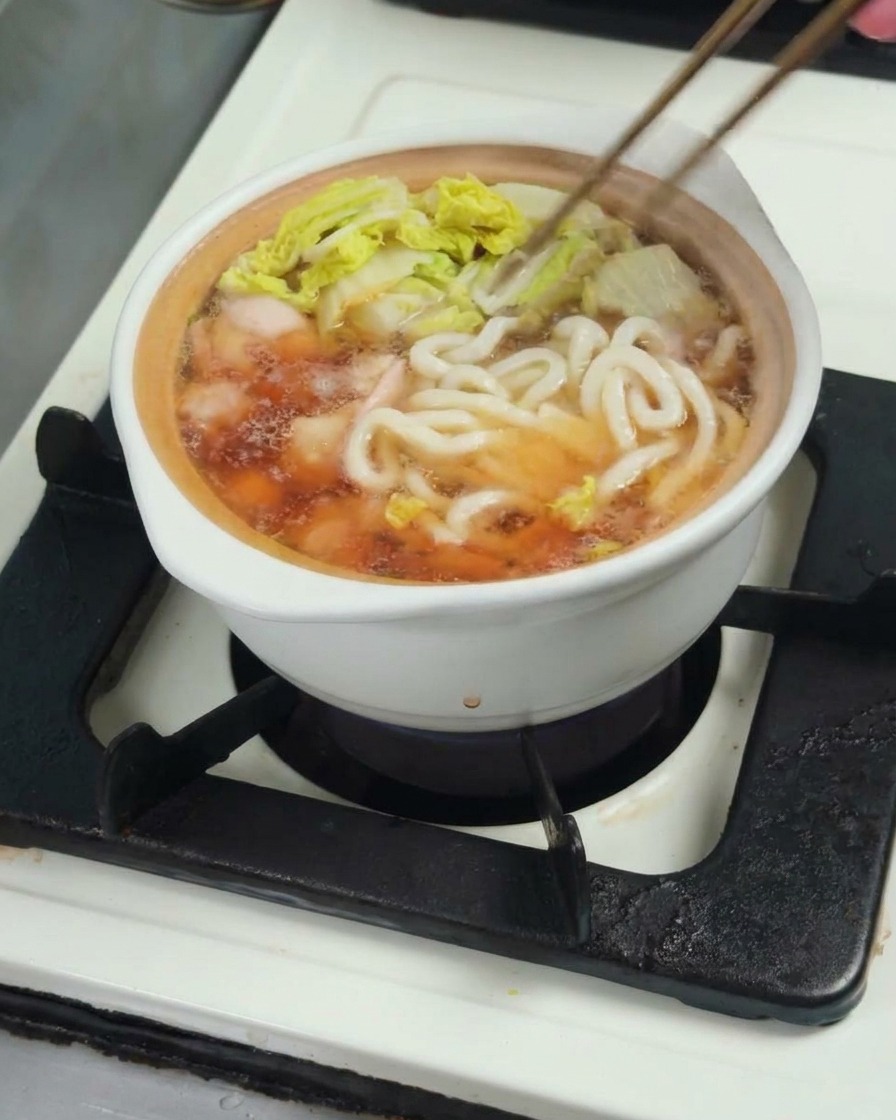 スープにうどんを入れ、鶏肉や野菜と一緒に煮込んでいる様子。