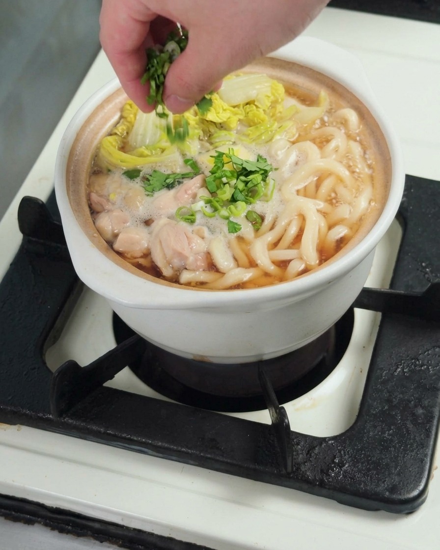 出来上がったうどんに、刻んだ小ねぎをトッピングしている様子。