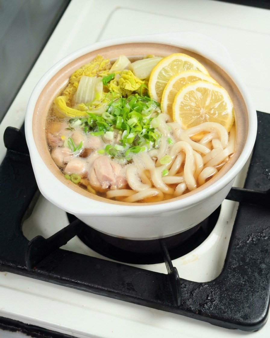 うどんの上に、薄くスライスした黄色いレモンを丁寧に並べている様子。