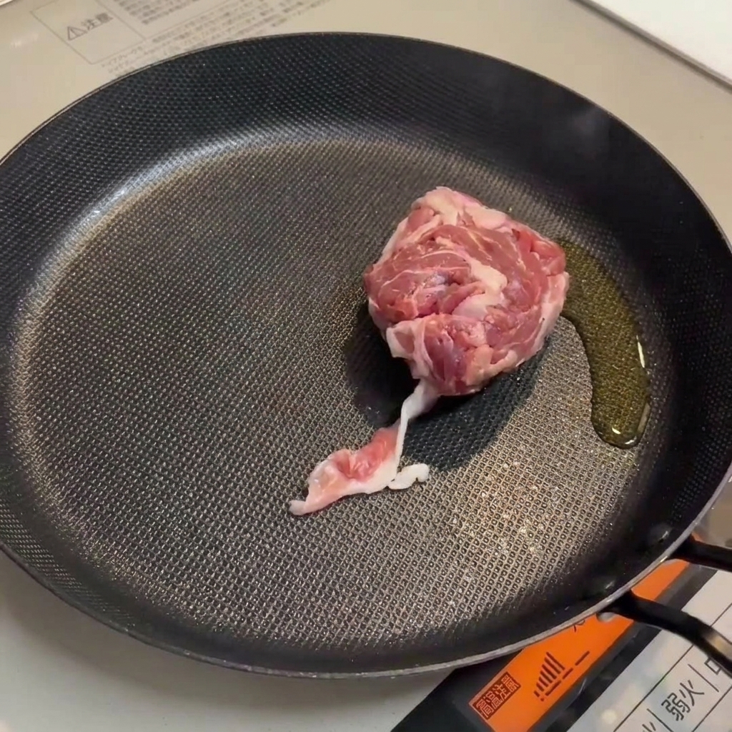 鍋で豚肉とソーセージが香ばしく焼けている様子。
