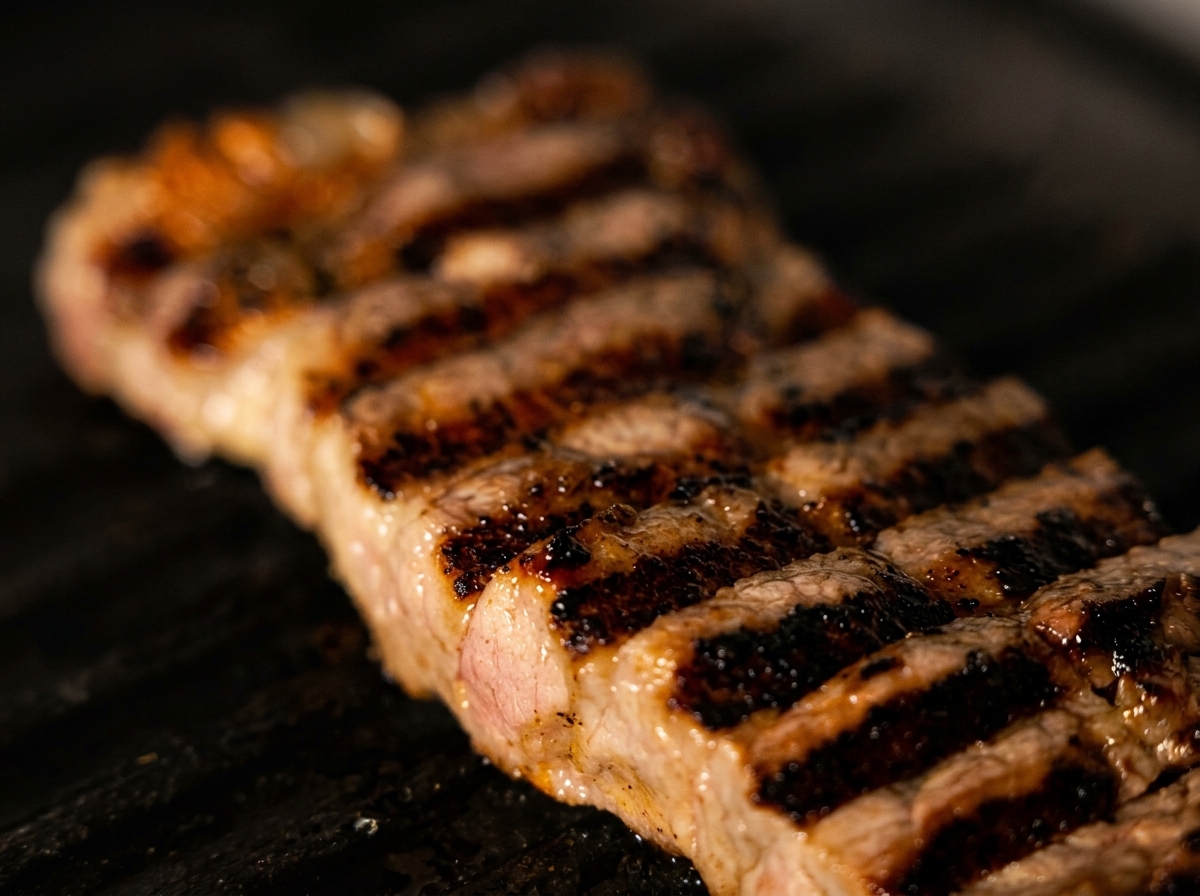 熱いグリルプレートで焼かれ、きれいな焼き目がついた厚切りのサーロインステーキのクローズアップ。