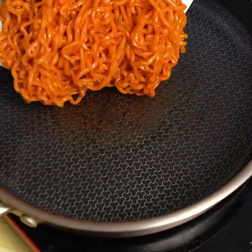 空の黒いフライパンに、ボウルから旨辛麺を入れている様子。