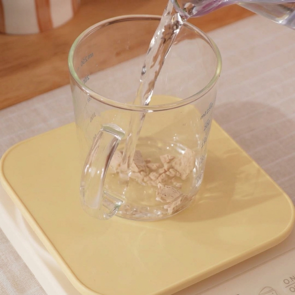 計量カップに入った氷水とイーストを小さな泡立て器で混ぜているアップ画像。