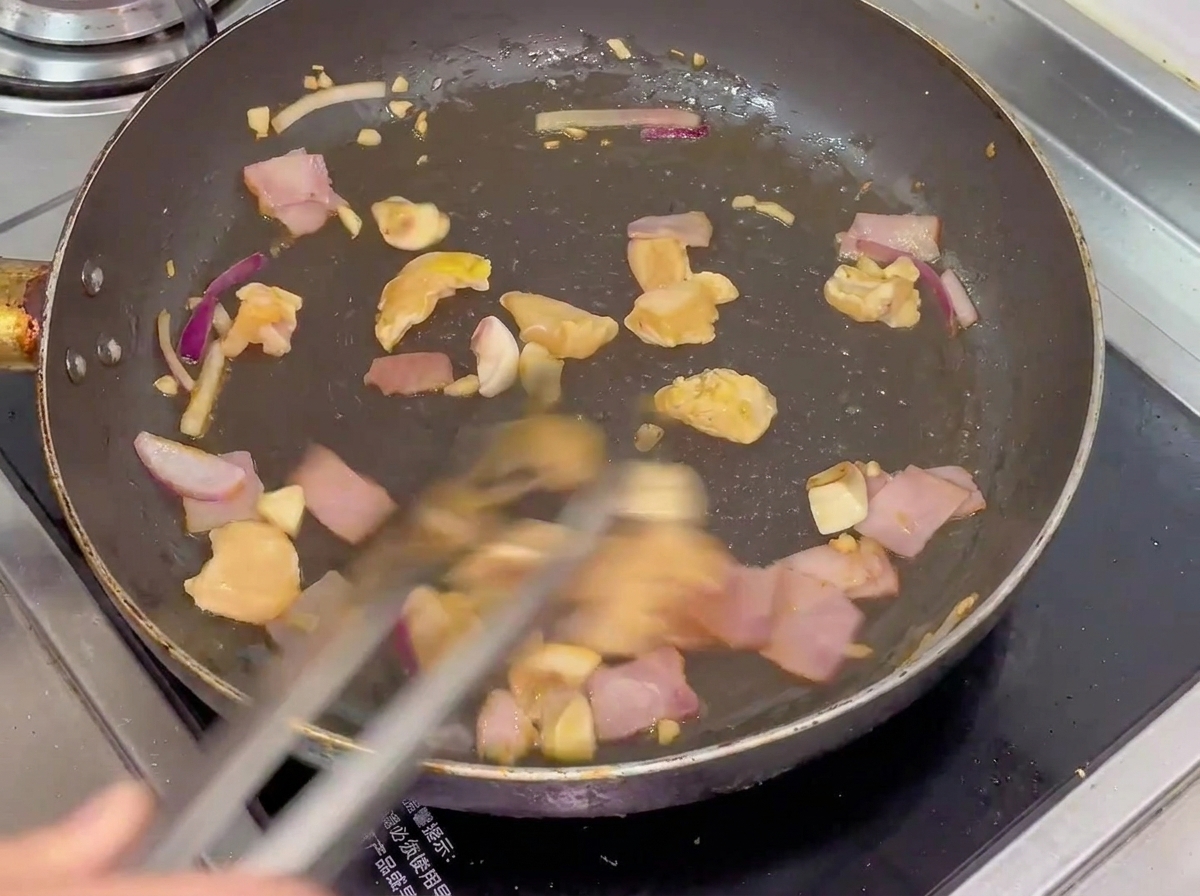 熱いフライパンで鶏肉、ベーコン、マッシュルーム、玉ねぎが炒められている様子。
