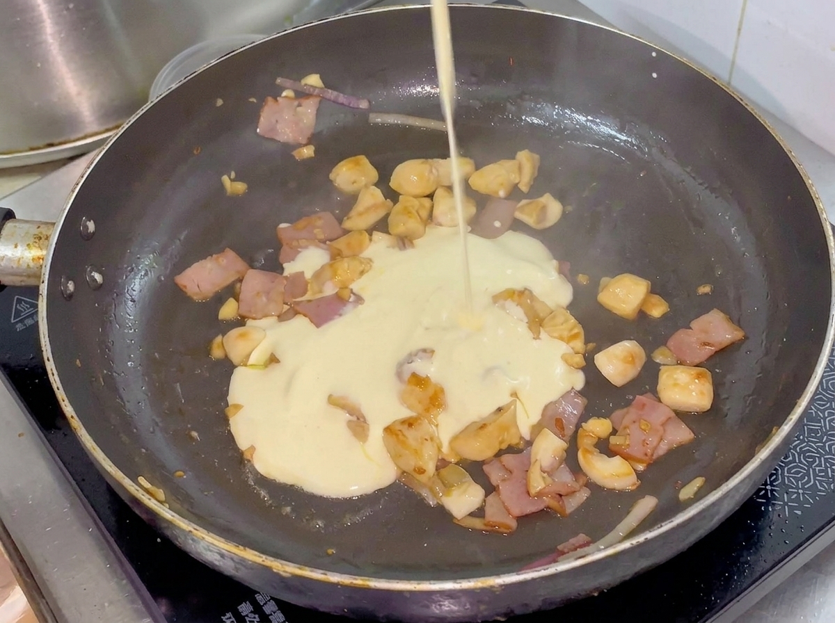鶏肉と野菜が入ったフライパンに、小さなピッチャーからクリームが注がれている様子。