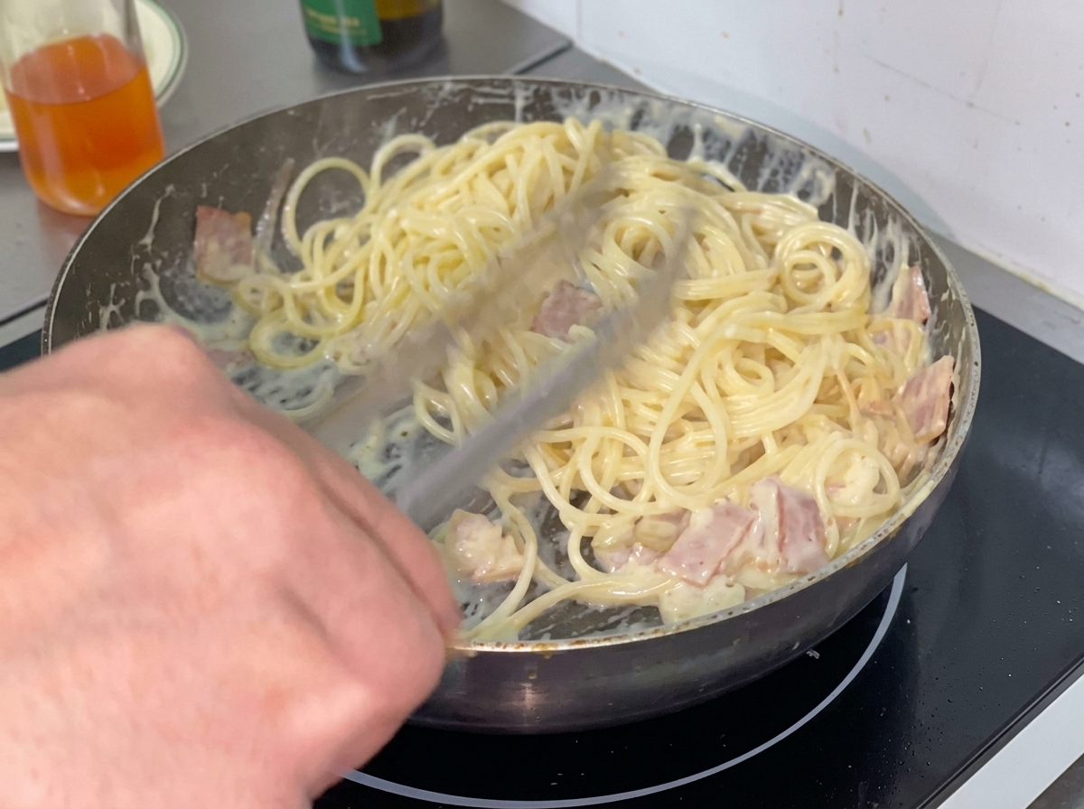 茹でたスパゲッティをクリームソースの入ったフライパンに入れている様子。
