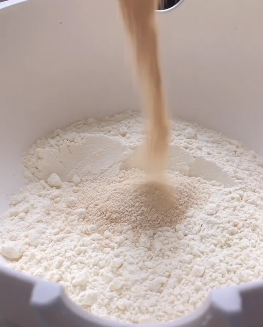 白い大きなボウルに入った小麦粉にドライイーストを加えている様子。