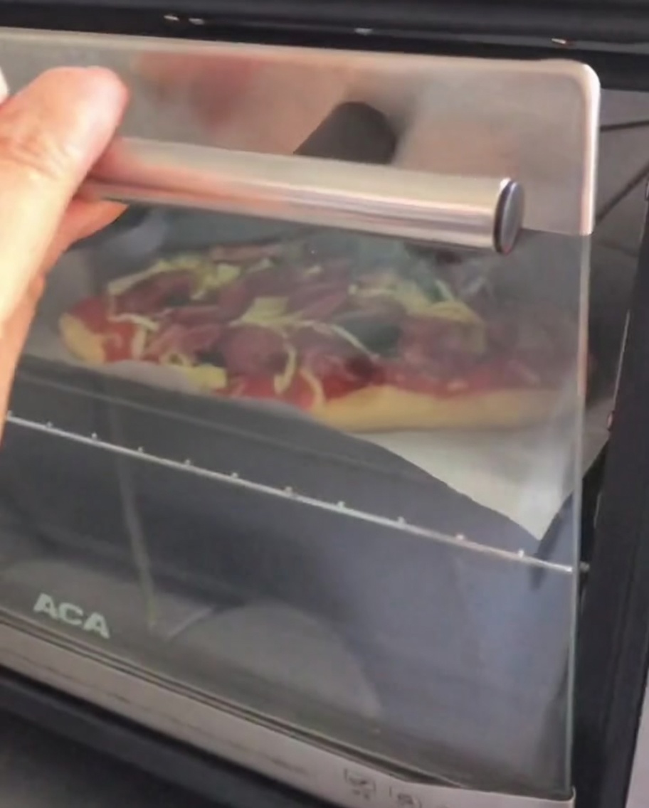 トッピングを終えた生のピザを天板にのせ、小型オーブンの扉を開けて中に入れている様子。