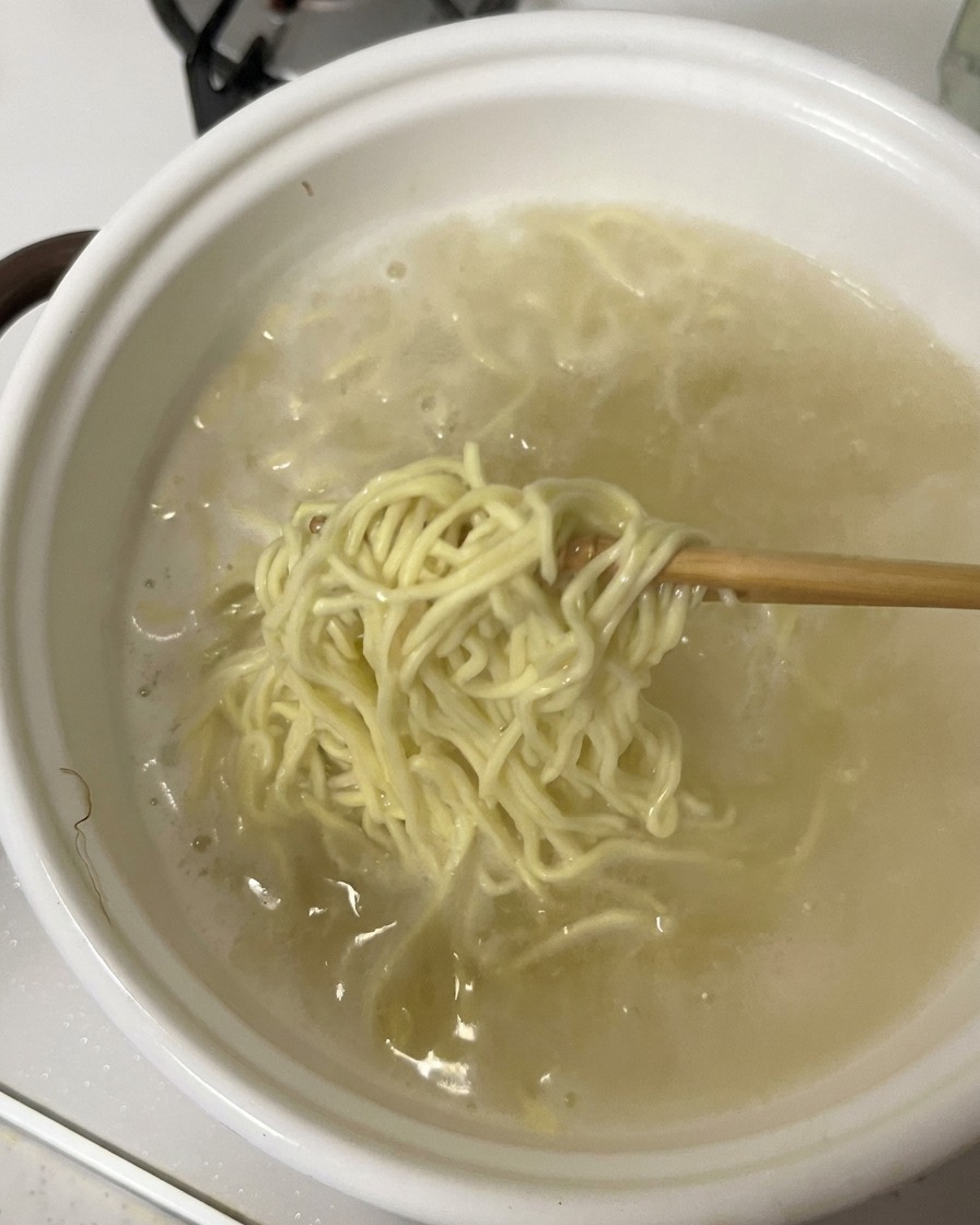 茹で上がった麺を箸で持ち上げ、丼に入れている様子。