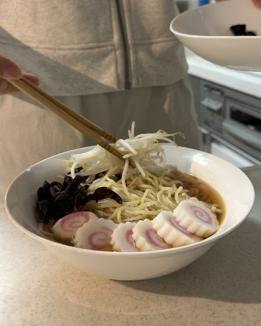 きくらげやなるとがのったラーメンに、もやしを丁寧に盛り付けている様子。