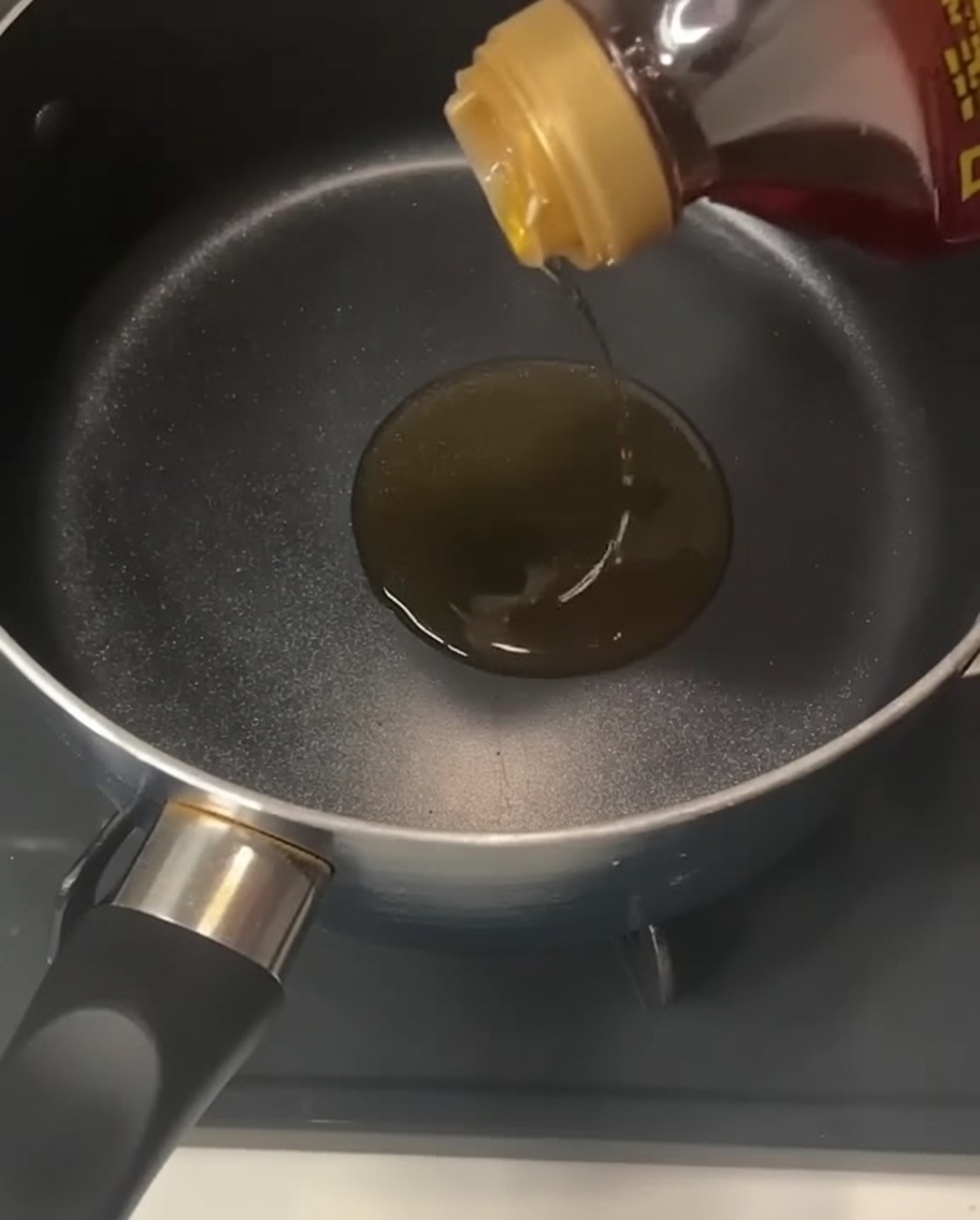 コンロの上の黒い鍋に、金色の透明なごま油を注いでいる様子。