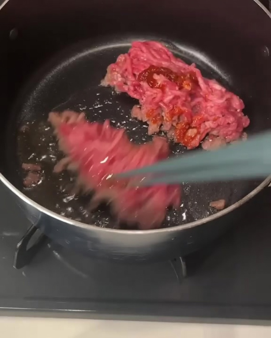 箸で挽き肉をほぐし、赤いチリペーストが絡まっている様子。