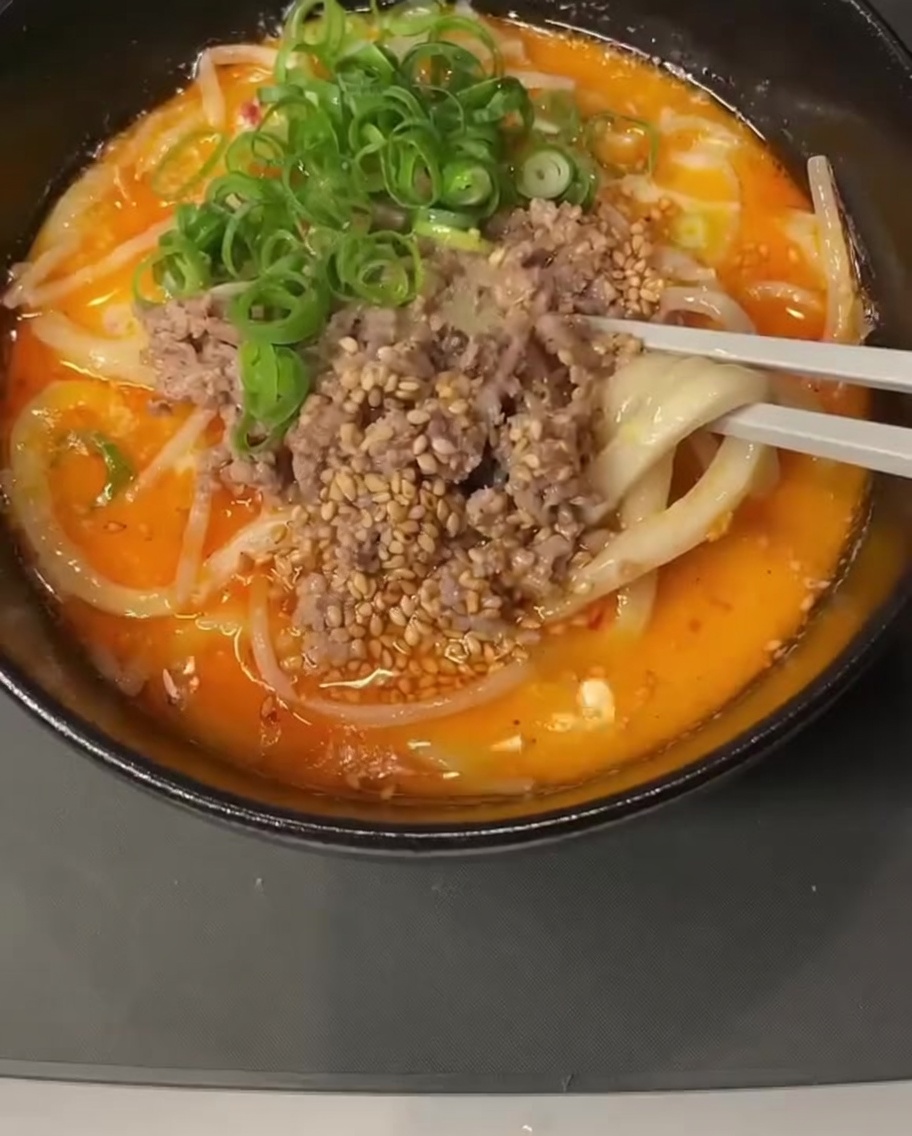クリーミーな液体が入った鍋に、スプーン一杯の味噌を溶かし入れている様子。