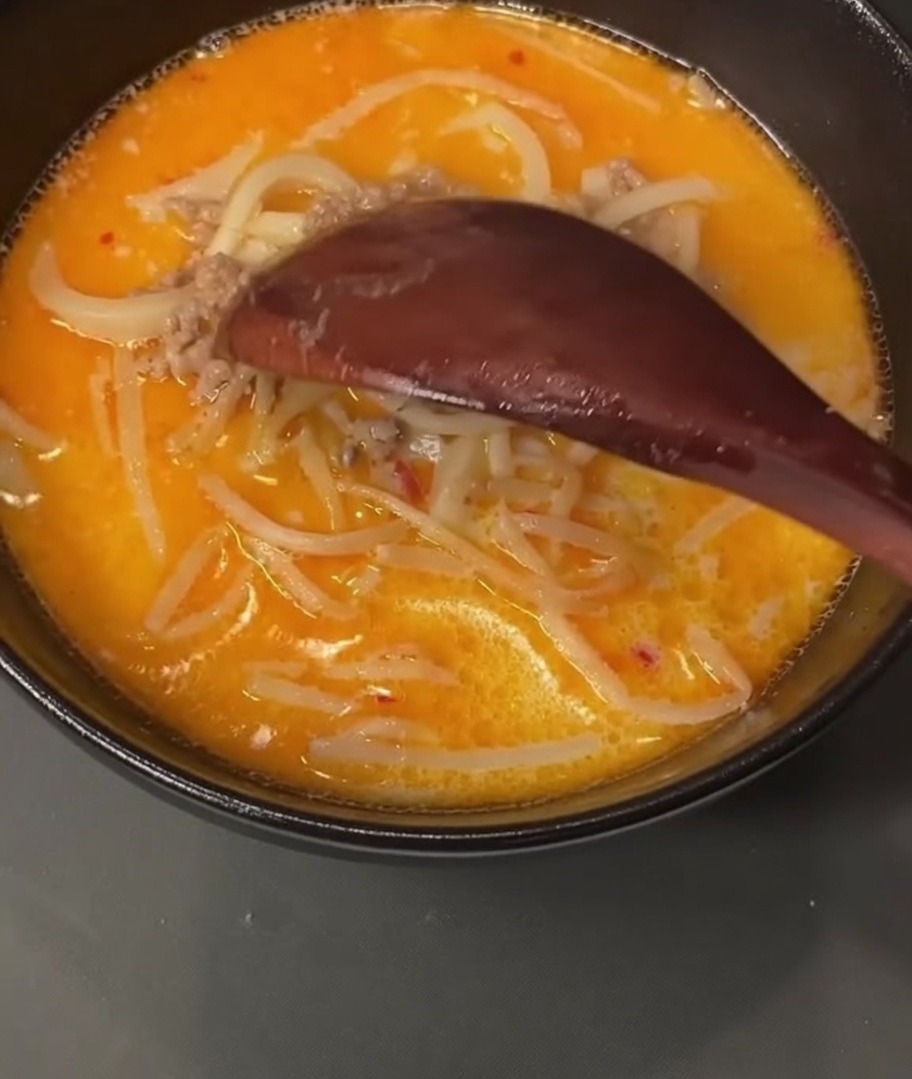 木製のスプーンで鍋の底から豚ひき肉をすくい上げている様子。