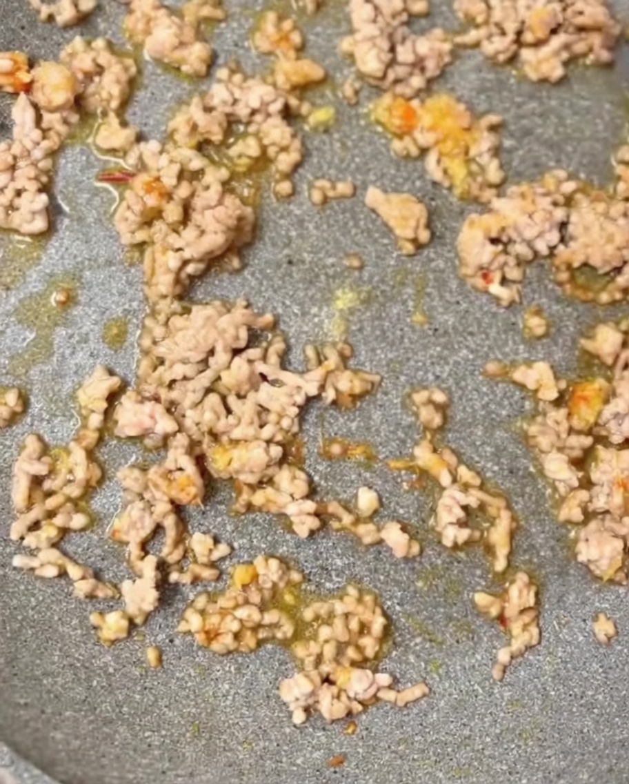 フライパンのひき肉に、すりごまや鶏ガラスープの素などの調味料を投入している様子。