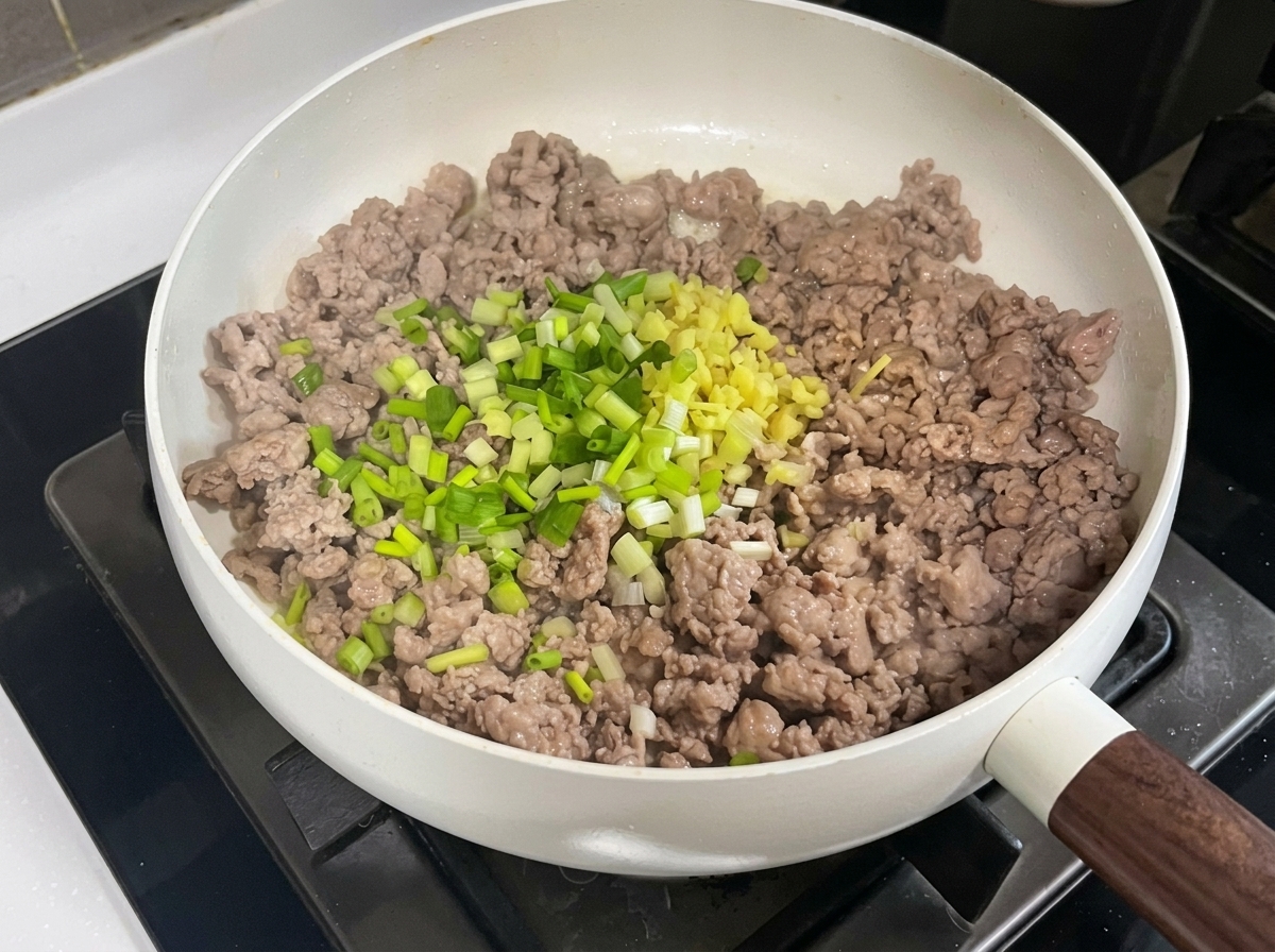 フライパンの中で、豚ひき肉とみじん切りにした香味野菜、豆板醤、甜麺醤を混ぜ合わせている様子。