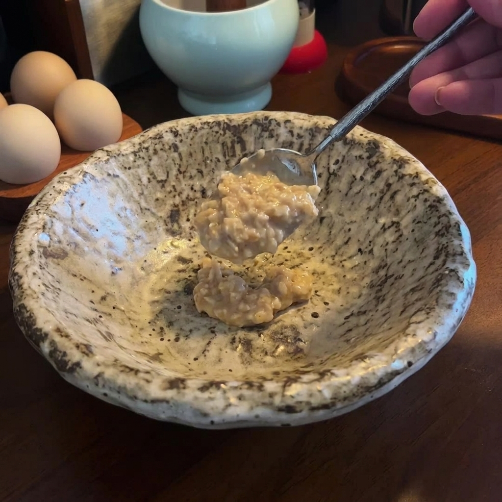 斑点模様のある陶器の器に、濃厚な味噌とごまペーストをスプーンで入れている様子。