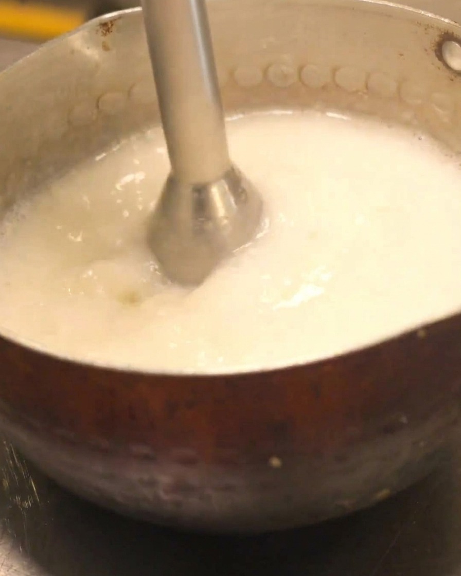 ハンドブレンダーを使って鶏白湯スープを泡立てている。