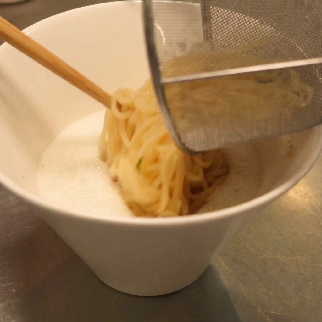 水気を切ったラーメン麺を、クリーミーなスープが入った器に移している。