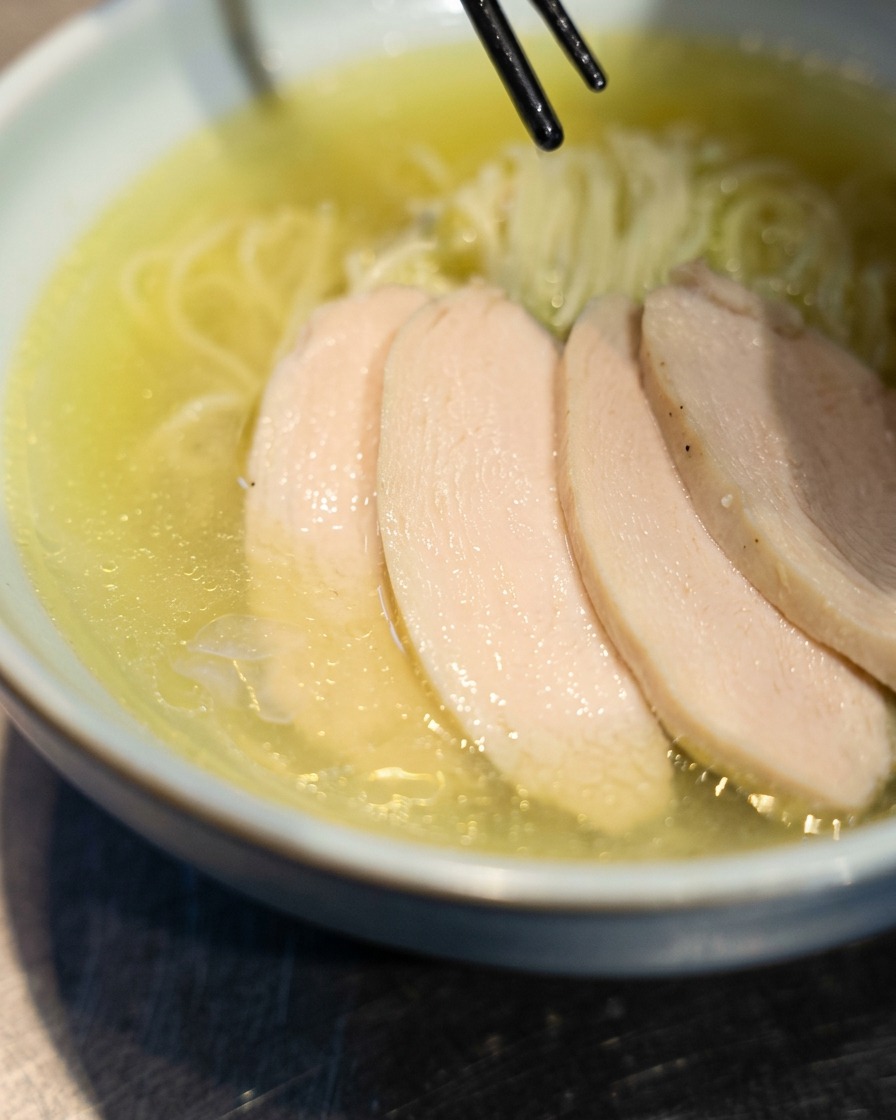 丼に盛られた麺の上に鶏チャーシュー、卵、ねぎを美しく盛り付けている様子。