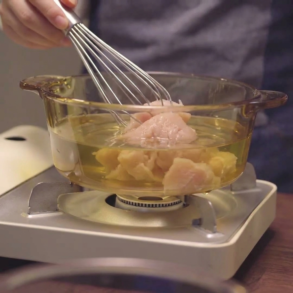 ガラス鍋の中で鶏ひき肉を泡立て器でかき混ぜている様子。