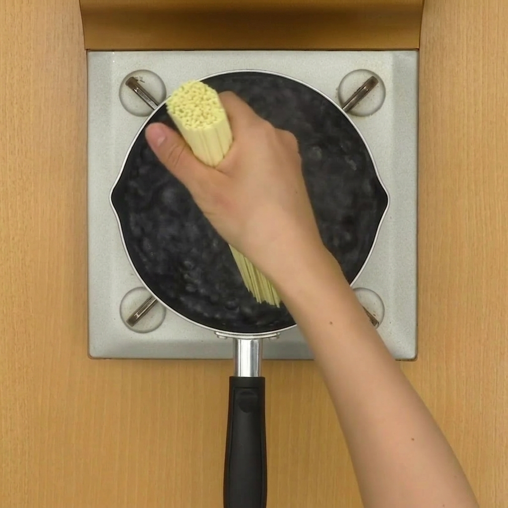 鍋で茹でられている中華麺を箸でほぐしている様子。