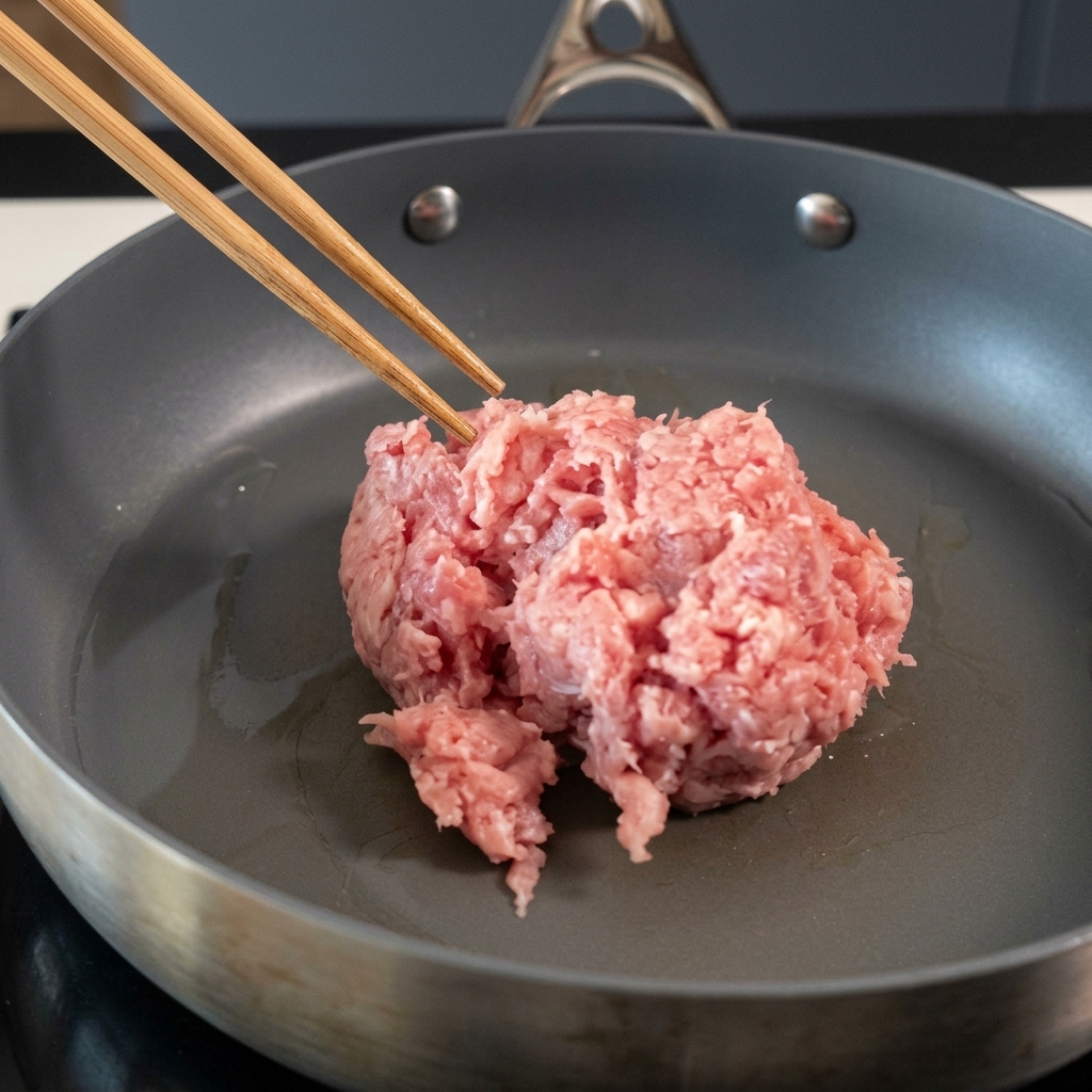 フライパンで箸を使って豚挽き肉を炒めている様子