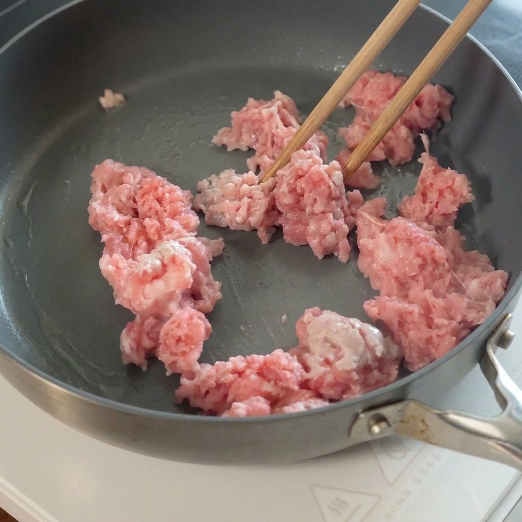 炒めた豚挽き肉にスライスしたニンニクを加えている様子