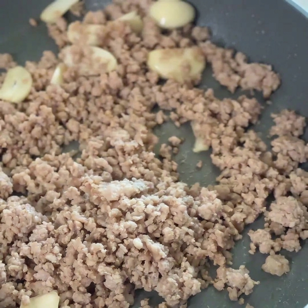 豚肉とニンニクに豆板醤を加えて混ぜている様子