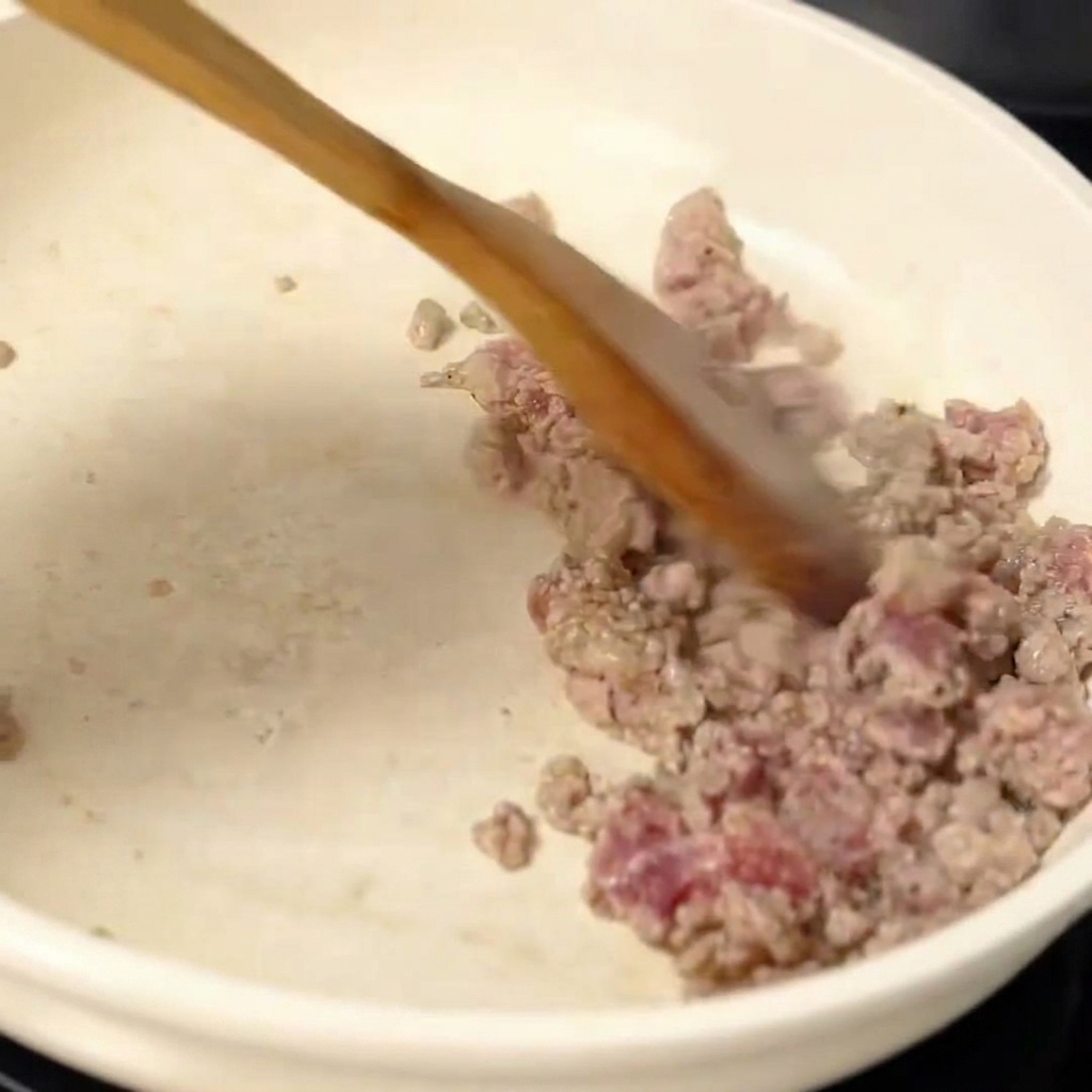 炒めたひき肉ににんにくを加えている様子。