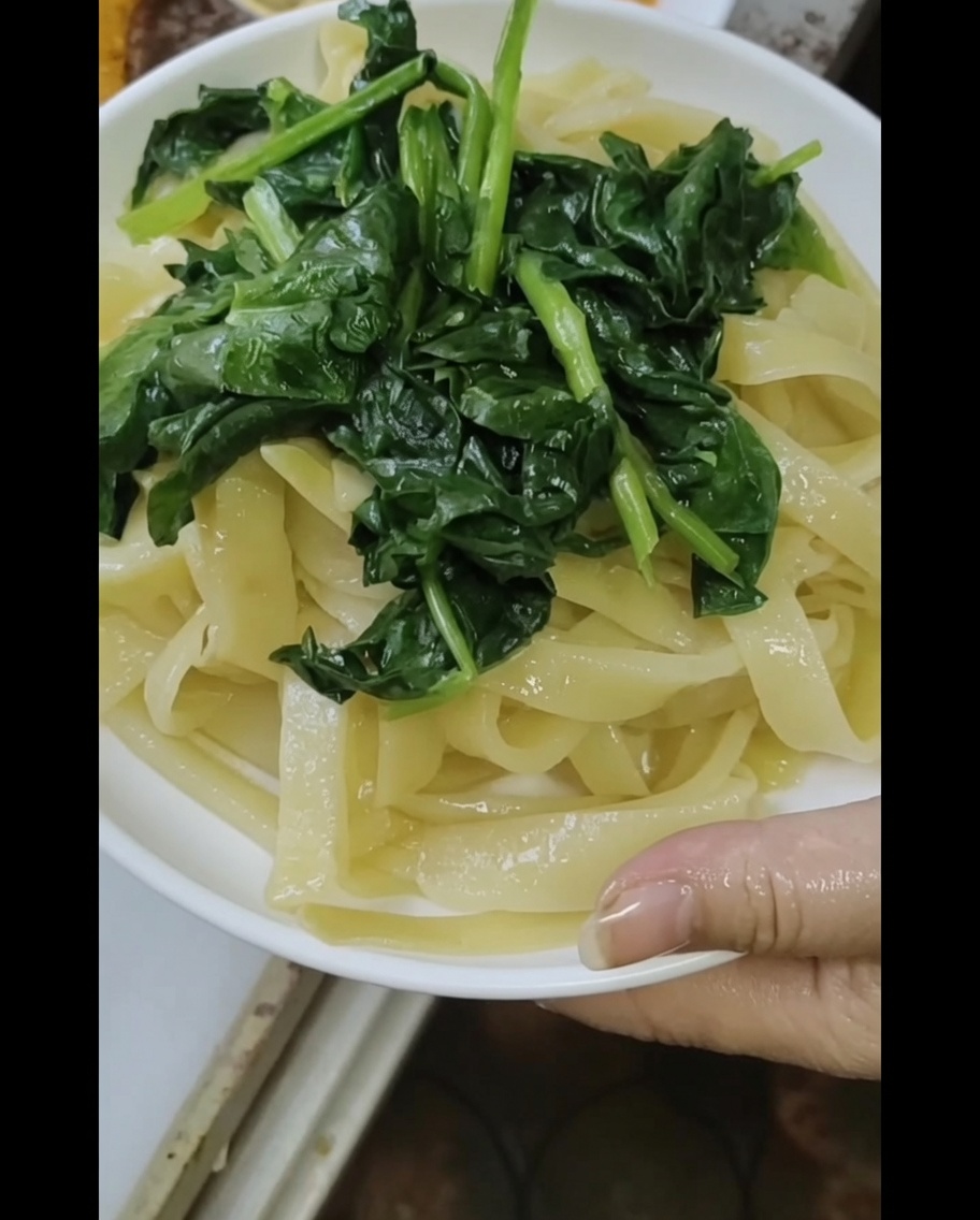 蒸し麺とほうれん草に、胡麻ピーナッツソースをかけているクローズアップショット。
