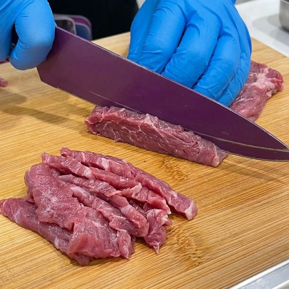 木のまな板の上で牛肩ロースを薄くスライスしている様子。