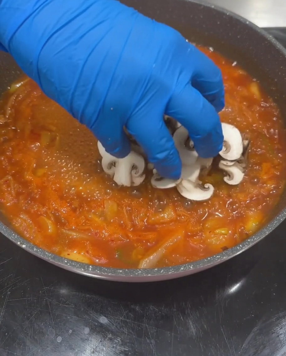 スライスしたしいたけ、ズッキーニ、豆腐を沸騰したキムチスープのベースに加えている様子。
