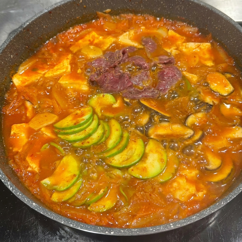 煮立っている野菜とキムチスープの入った鍋に、マリネした牛肉を入れている様子。