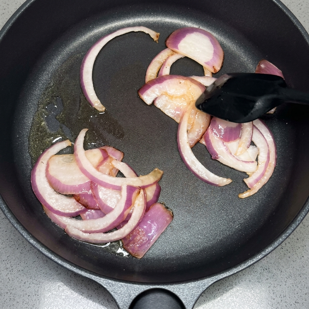 スパチュラで鍋の中の赤玉ねぎのスライスを炒めている様子。