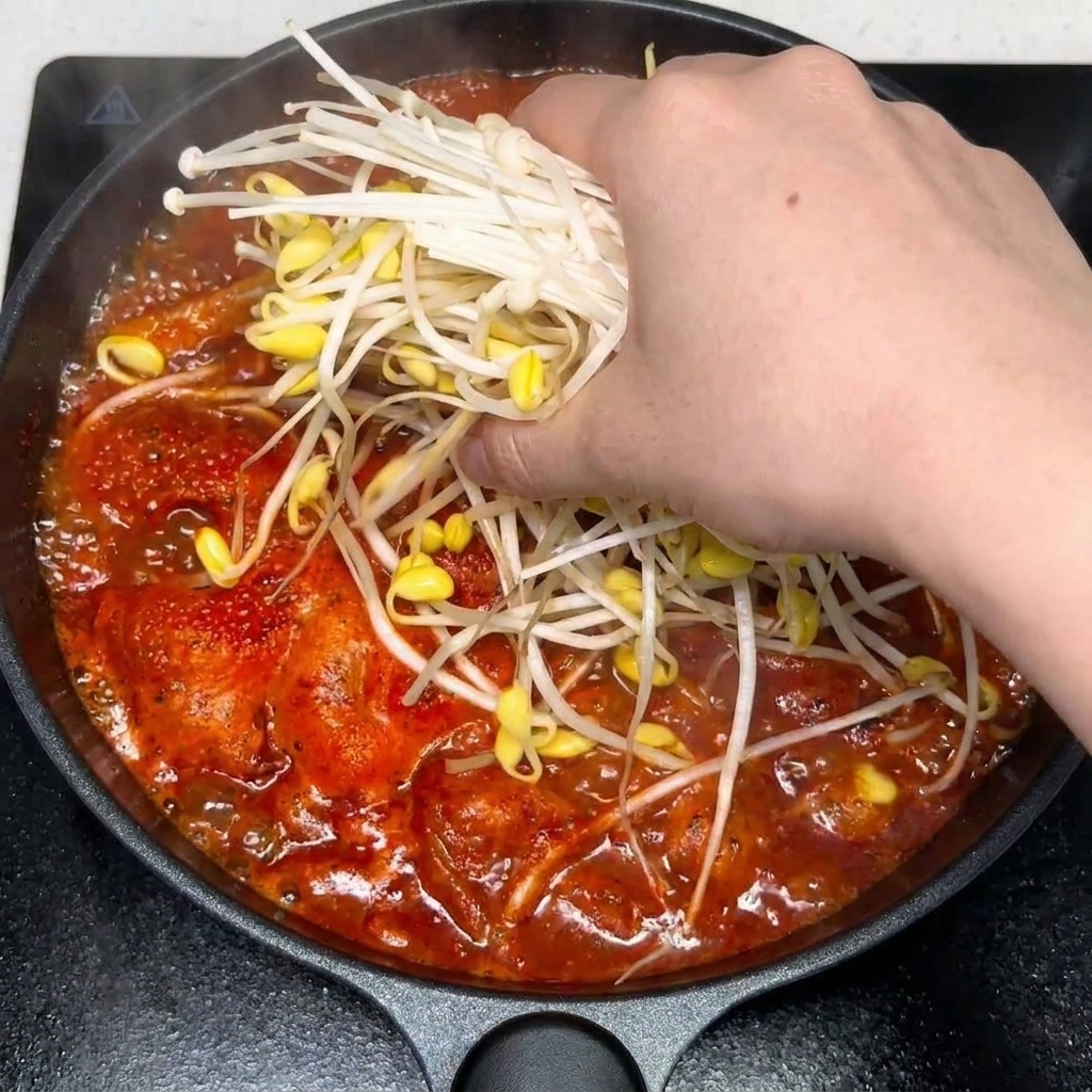 赤いピリ辛キムチスープに、おろしにんにくと調味料を混ぜている様子。