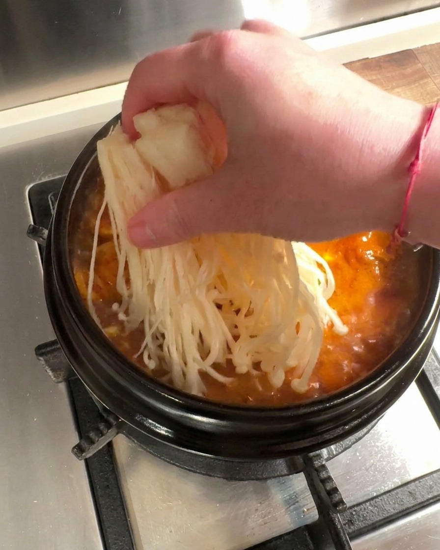沸騰した赤いスープにえのき茸と生の牛肉を加えている様子。